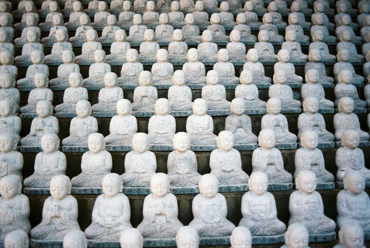 Stillness in repetition. Rows of identical stone Buddha statues arranged in perfect symmetry, symbolizing the quiet rhythm and structure found within repetition.
