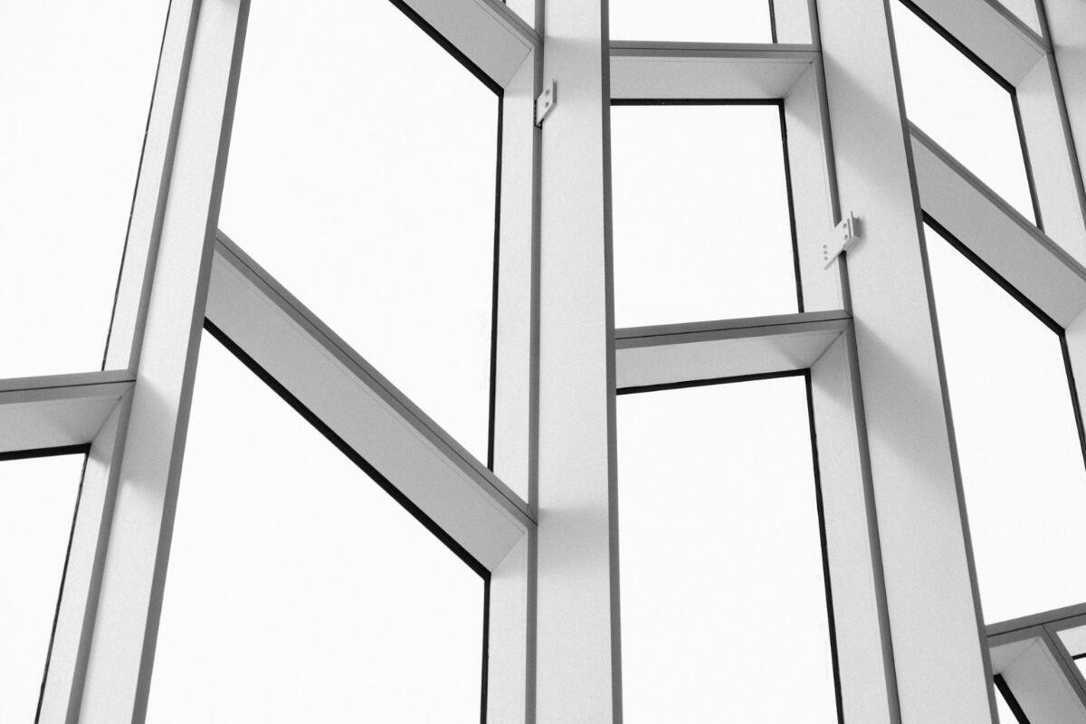 Fragility in Structure Minimalist architectural grid of intersecting white window frames against a bright background, symbolizing structure, alignment, and fragility within complex systems.