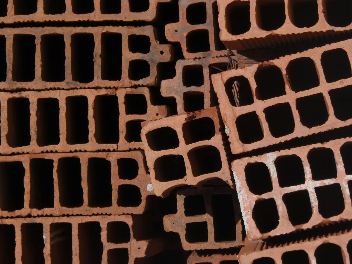 Close-up of stacked hollow clay bricks forming a dense grid, representing the weight and repetition of growth-driven systems that strain under their own design.