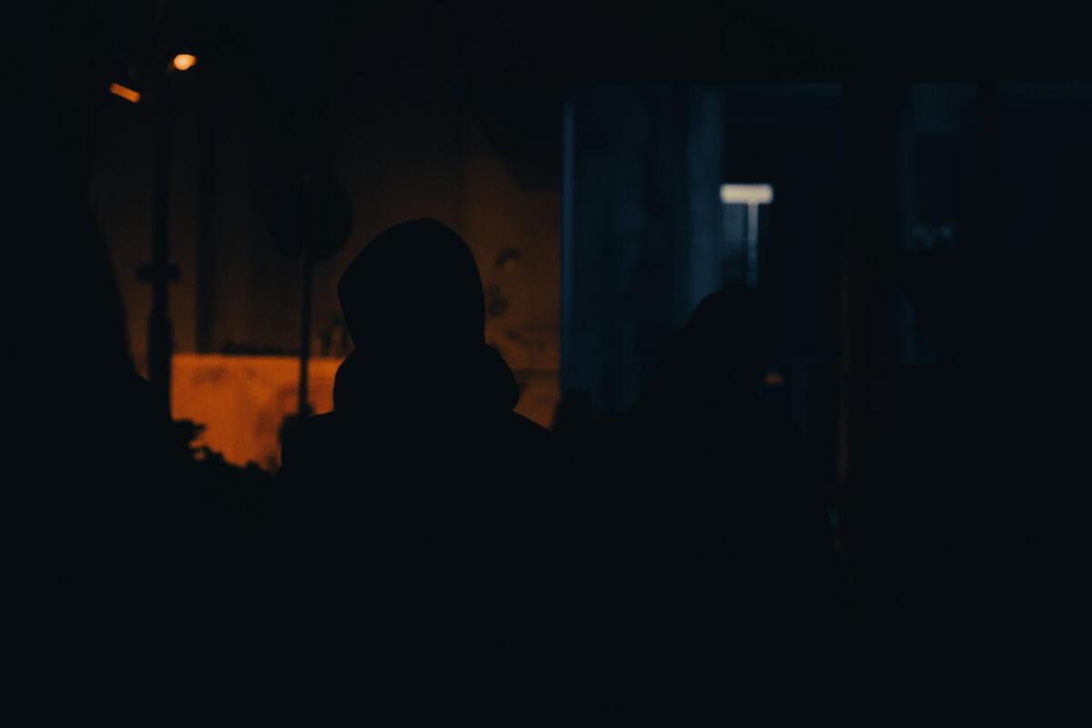 Silhouette in the dark A dark silhouette of a person in a hoodie standing in a dimly lit street at night, illuminated by warm streetlights — capturing solitude, reflection, and the unseen journey forward.