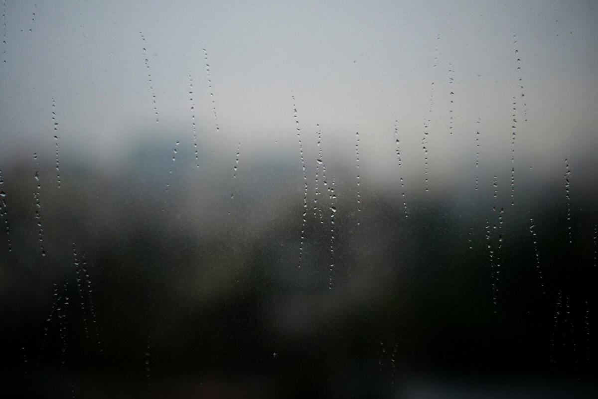 Raindrops streaking down a foggy window, blurring the cityscape beyond and creating a sense of distance and introspection.